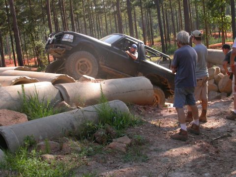 1990 Ford Bronco - A black truck maneuvers through a challenging obstacle course made of concrete pipes in a forest setting.