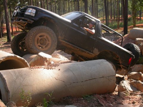 1990 Ford Bronco - A modified 1990 Ford Bronco navigates a challenging off-road course with large concrete pipes and rocks.