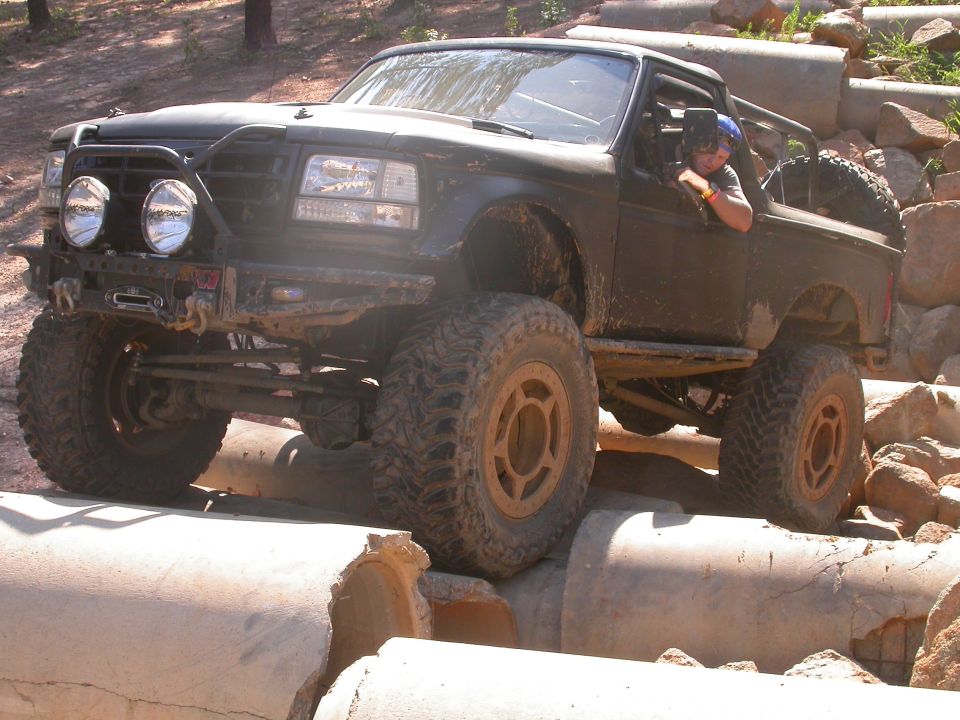 Modified 1990 Ford Bronco with large tires navigating concrete pipes off-road