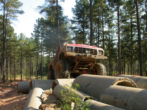 1990 Ford Bronco - Off-road truck navigating concrete pipes in a wooded area. Grille suggests an older model.