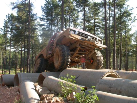 1990 Ford Bronco - An off-road vehicle navigates a challenging obstacle course made of concrete pipes in a wooded area.