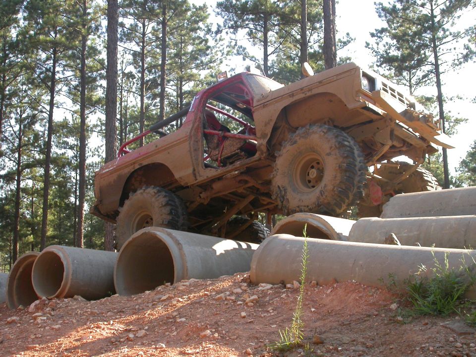muddy off-road truck with roll cage driving over concrete pipes in a wooded area