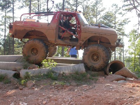 1990 Ford Bronco - This heavily modified SUV, likely a 1978 Ford Bronco, tackles a challenging off-road course with large tires and a protective roll cage.