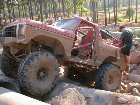 1990 Ford Bronco - This heavily modified SUV is navigating a challenging obstacle course with large rocks and concrete pipes.