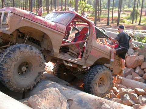 1990 Ford Bronco - This heavily modified off-road SUV is tackling a challenging terrain of rocks and logs.