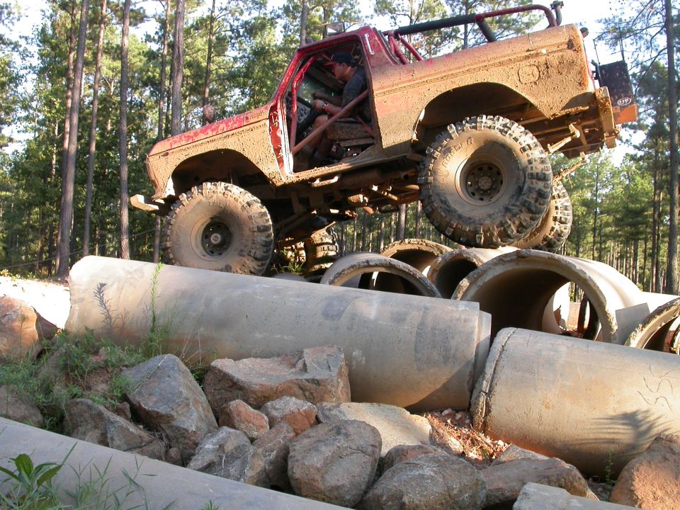 1990 Ford Bronco climbing over concrete pipes, covered in mud