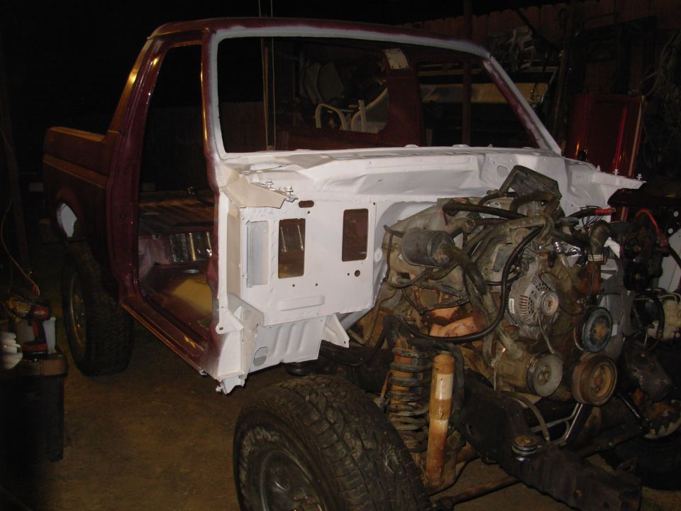 Maroon Ford truck mid-restoration with white-primed firewall and exposed engine in a shop.