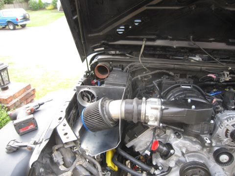 2008 Jeep Wrangler - The engine bay of a Jeep shows an aftermarket air intake system being installed, with a cordless drill visible on the fender.