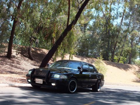 2003 Ford Crown Victoria - Front three-quarter shot of a lowered black sedan with grille guard and blacked-out wheels.