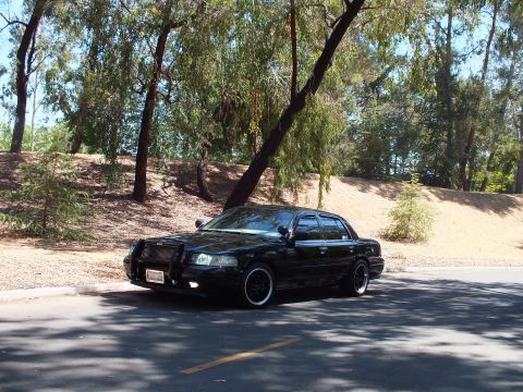2003 Ford Crown Victoria - Profile-front angle of a black full-size sedan with push bar and lowered stance.