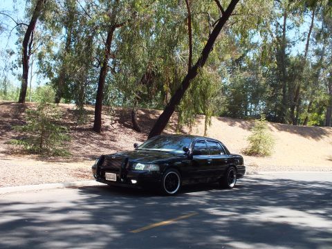 2003 Ford Crown Victoria - Black Mercury Grand Marquis shown from the front left on a tree-shaded roadway.