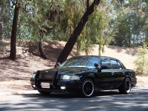 2003 Ford Crown Victoria - Front-quarter view of a black Mercury Grand Marquis beneath willow branches.