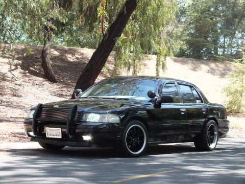 2003 Ford Crown Victoria - Close front-quarter view of a black sedan with push bar and staggered wheels.
