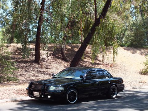 2003 Ford Crown Victoria - Front-left view of a black Mercury Grand Marquis on a tree-lined road.