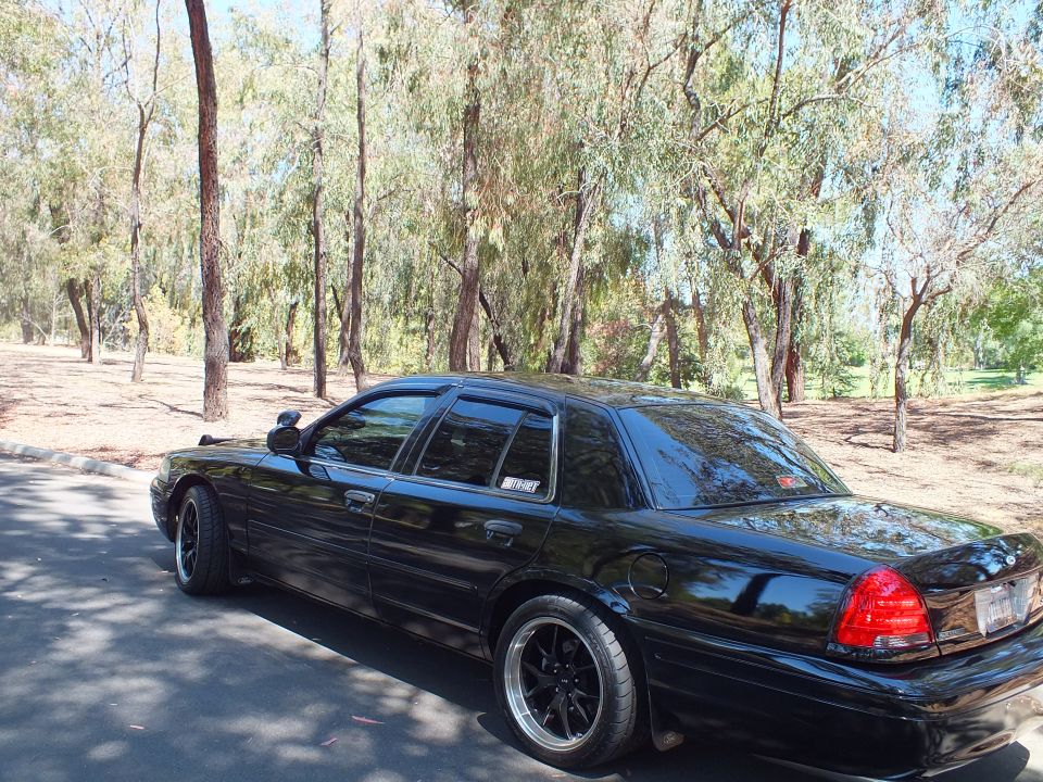 Rear side view of a black Ford Crown Victoria lowered on black wheels in a park