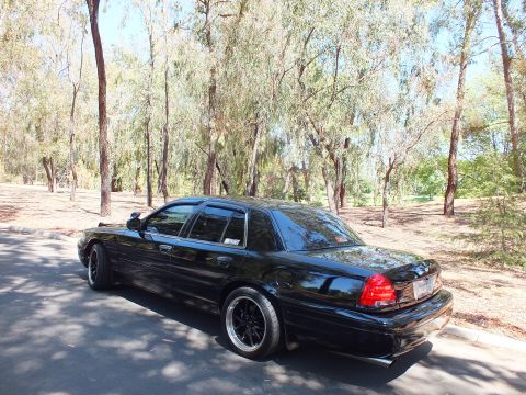 2003 Ford Crown Victoria - Rear three-quarter view of a black Crown Victoria parked among bare trees.