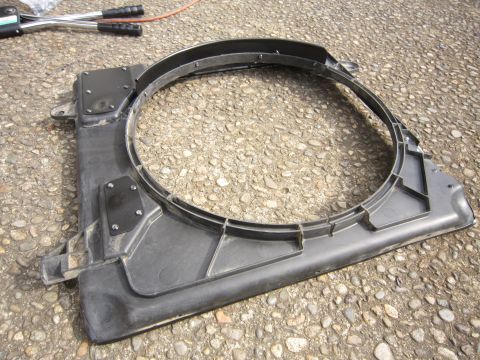 2008 Jeep Wrangler - A black plastic radiator fan shroud is shown lying on a gravel surface, with tools visible in the upper left corner.
