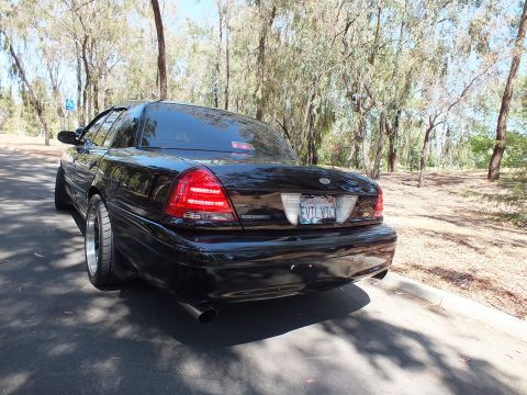 2003 Ford Crown Victoria - Rear-quarter shot of a black full-size sedan parked beside a dry leaf-covered slope.