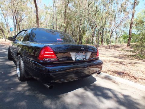 2003 Ford Crown Victoria - Blacked-out full-size sedan shown from the rear with visible exhaust outlet.