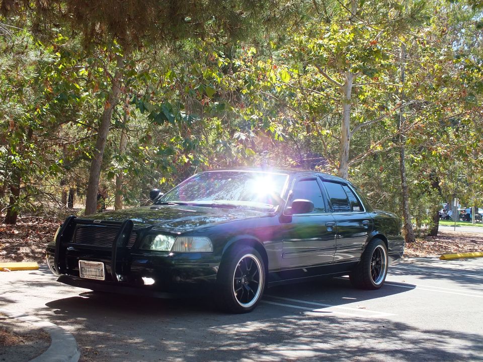 Black Ford Crown Victoria with grille guard and spotlight in a shaded parking lot