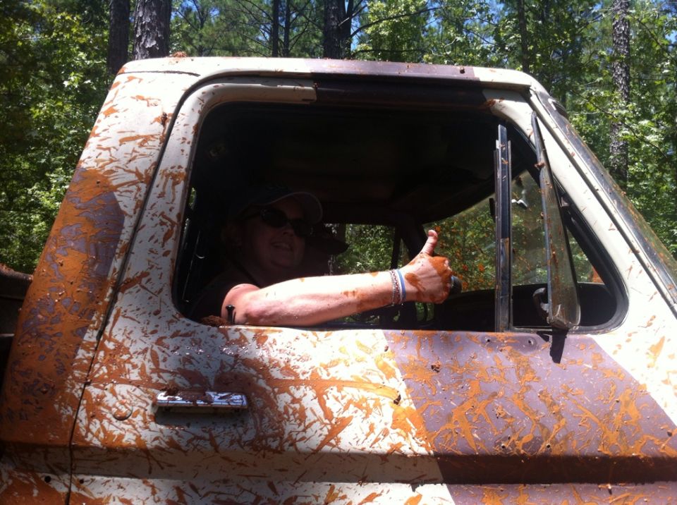 Muddy truck cab with driver giving a thumbs up. The vehicle is covered in brown mud splatters