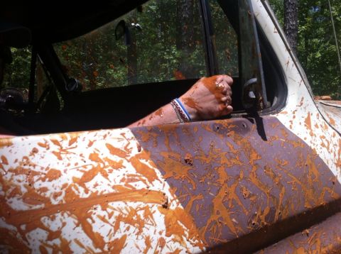 1979 Ford F-150 - A person's arm, covered in mud, rests on the side of a heavily mud-splattered truck.