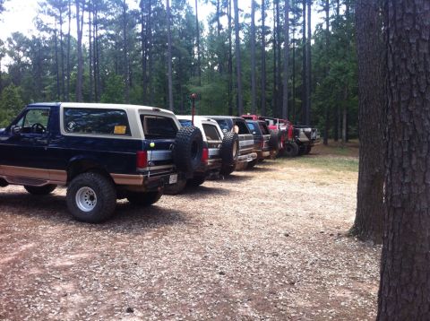1979 Ford F-150 - A line of off-road vehicles, including a Ford Bronco, are parked in a wooded area.