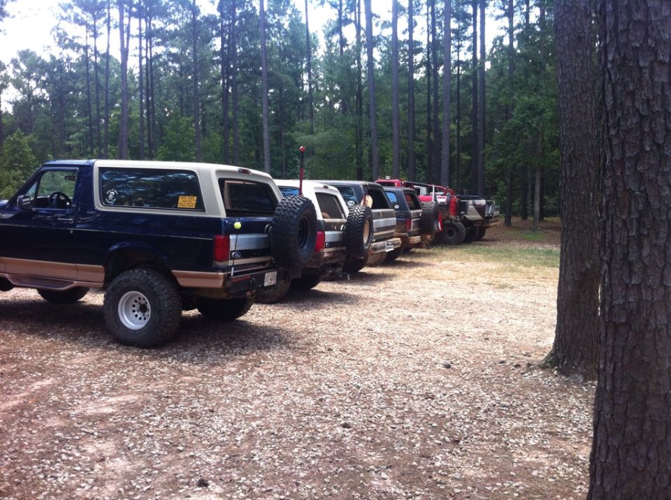 Dark blue and tan Ford Bronco with a spare tire mounted on the rear, parked in a line with other off-road vehicles