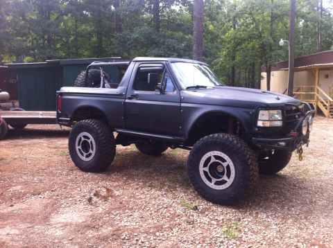 1979 Ford F-150 - This modified black Ford Bronco features off-road tires and a roll cage, parked outdoors.