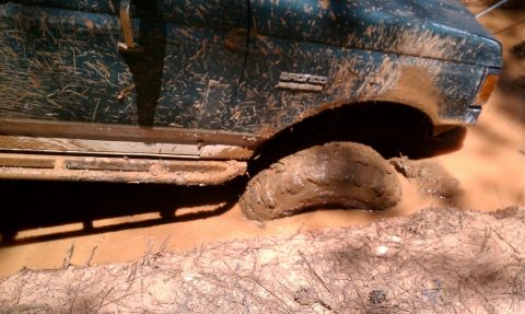 1979 Ford F-150 - A mud-covered Ford Bronco is stuck in a muddy puddle, with its front right tire deep in the mire.