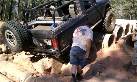 1979 Ford F-150 - A modified black truck is seen maneuvering through a challenging obstacle course of concrete pipes and rocks.