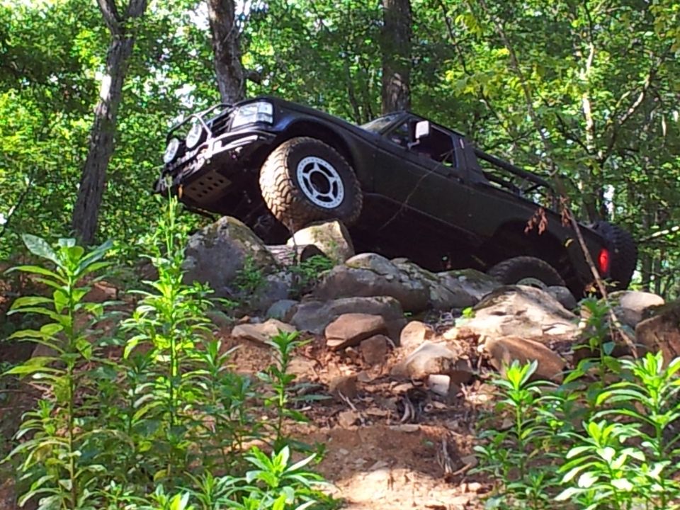 Black off-road truck with large tires climbing over rocks on a wooded trail