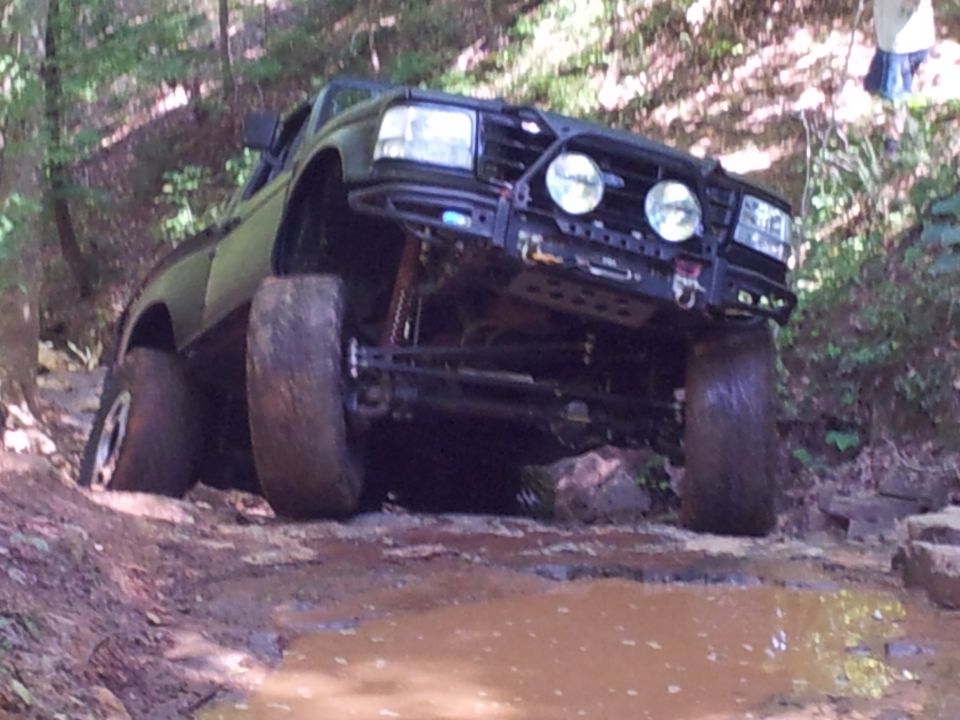 Black off-road truck with large tires navigating a muddy trail with rocks