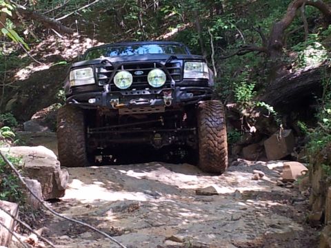 1979 Ford F-150 - A modified black Ford F-150 navigates a challenging rocky path through a wooded area.
