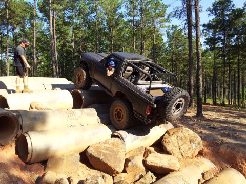 1979 Ford F-150 - A modified black truck tackles an obstacle course made of concrete pipes and rocks in a wooded area.