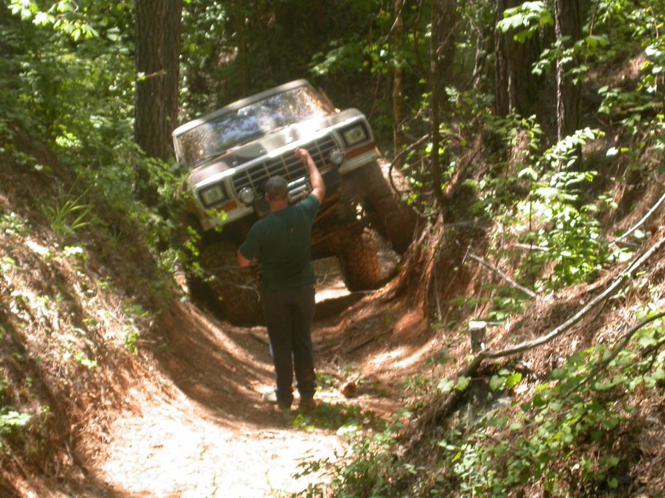 Man standing by a 1979 Ford F-150 as it goes down a steep, wooded ditch