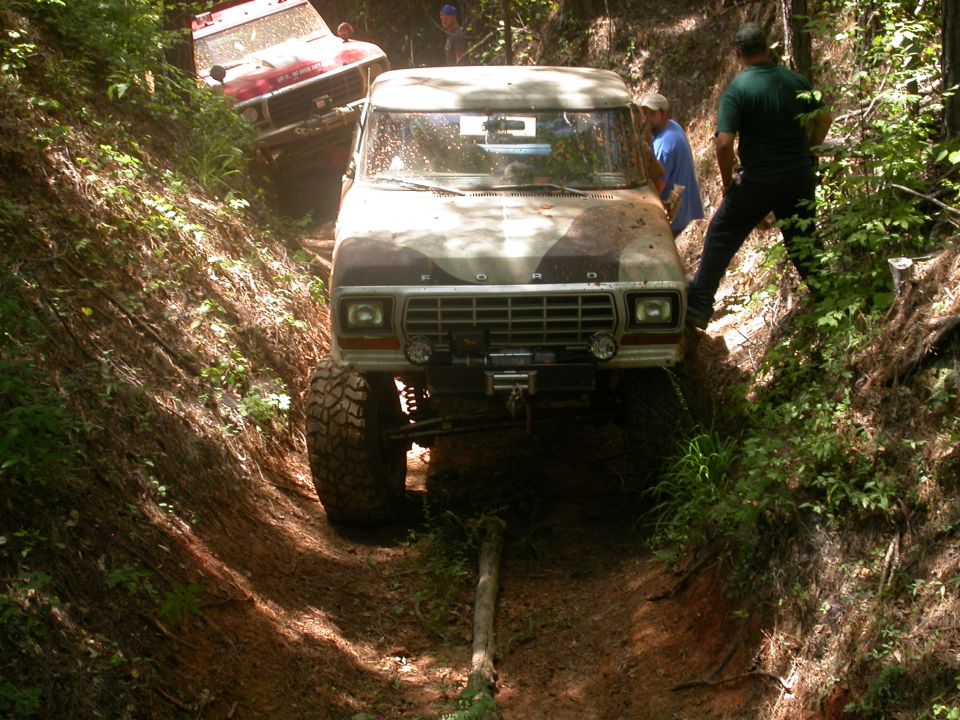 Front view of a 1979 Ford F-150 on a muddy trail, with another vehicle behind it