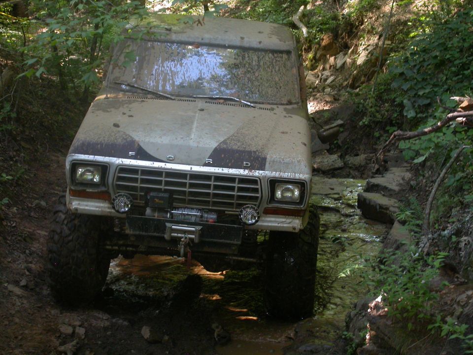 Mud-covered 1979 Ford F-150 driving through a creek with large tires and a winch