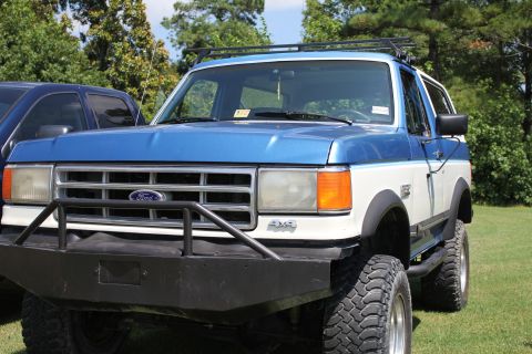 1994 Ford Bronco - This blue and white 1994 Ford Bronco features an aftermarket bumper and roof rack, parked outdoors.