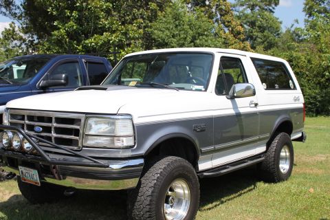 1994 Ford Bronco - This 1994 Ford Bronco is parked on grass with a blue truck beside it.