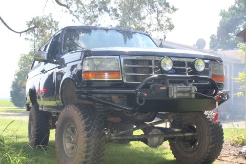 1994 Ford Bronco - Lifted 1994 Ford Bronco with a custom front bumper and winch sits on grassy terrain.