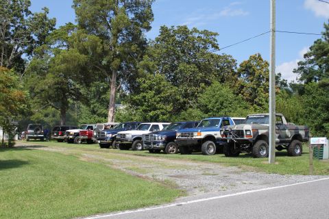1994 Ford Bronco - Several lifted Ford trucks are parked in a row on a sunny day.