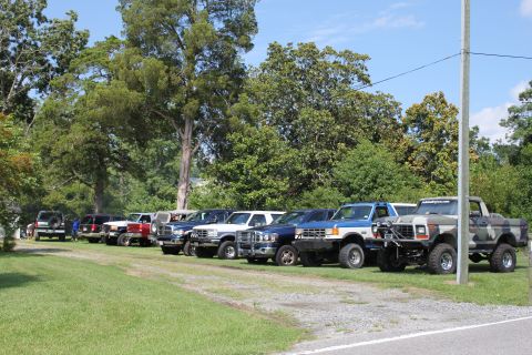 1994 Ford Bronco - A row of Ford Broncos and trucks are parked on a grassy area under a clear blue sky.