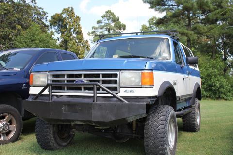 1994 Ford Bronco - Modified Ford Bronco with custom front bumper and roof rack sits on a grassy field next to another vehicle.