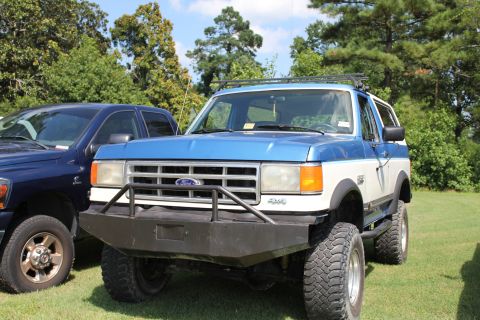 1994 Ford Bronco - A two-tone Ford Bronco is parked on a grassy field with trees in the background.