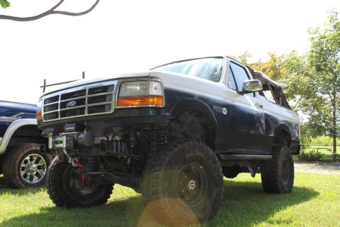 1994 Ford Bronco - A modified Ford Bronco sits on a grassy field next to another vehicle under a bright sky.