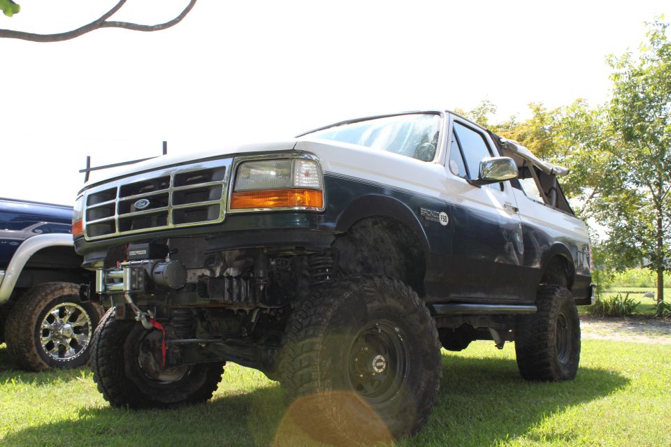 Two-tone Ford Bronco with lifted suspension and winch, parked on grass