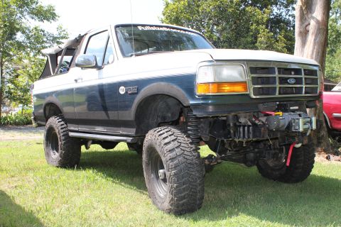 1994 Ford Bronco - This lifted 1994 Ford Bronco features a winch and off-road tires, parked on a grassy area.