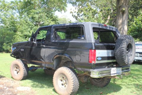 1994 Ford Bronco - This lifted Ford Bronco is parked on grass with trees in the background. A second vehicle is partially visible.