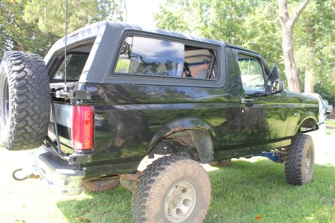 1994 Ford Bronco - Side view of a black 1994 Ford Bronco with a lifted suspension and a spare tire on the back.